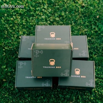 Several black boxes labeled 'Training Box' are stacked on a grassy surface. The top box features illustrations of a kettlebell and a dumbbell.